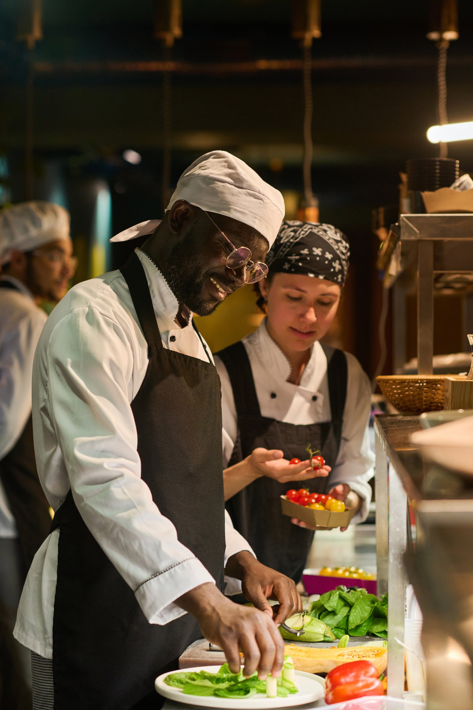 Happy young African American male chef mixing fresh ingrdients on board