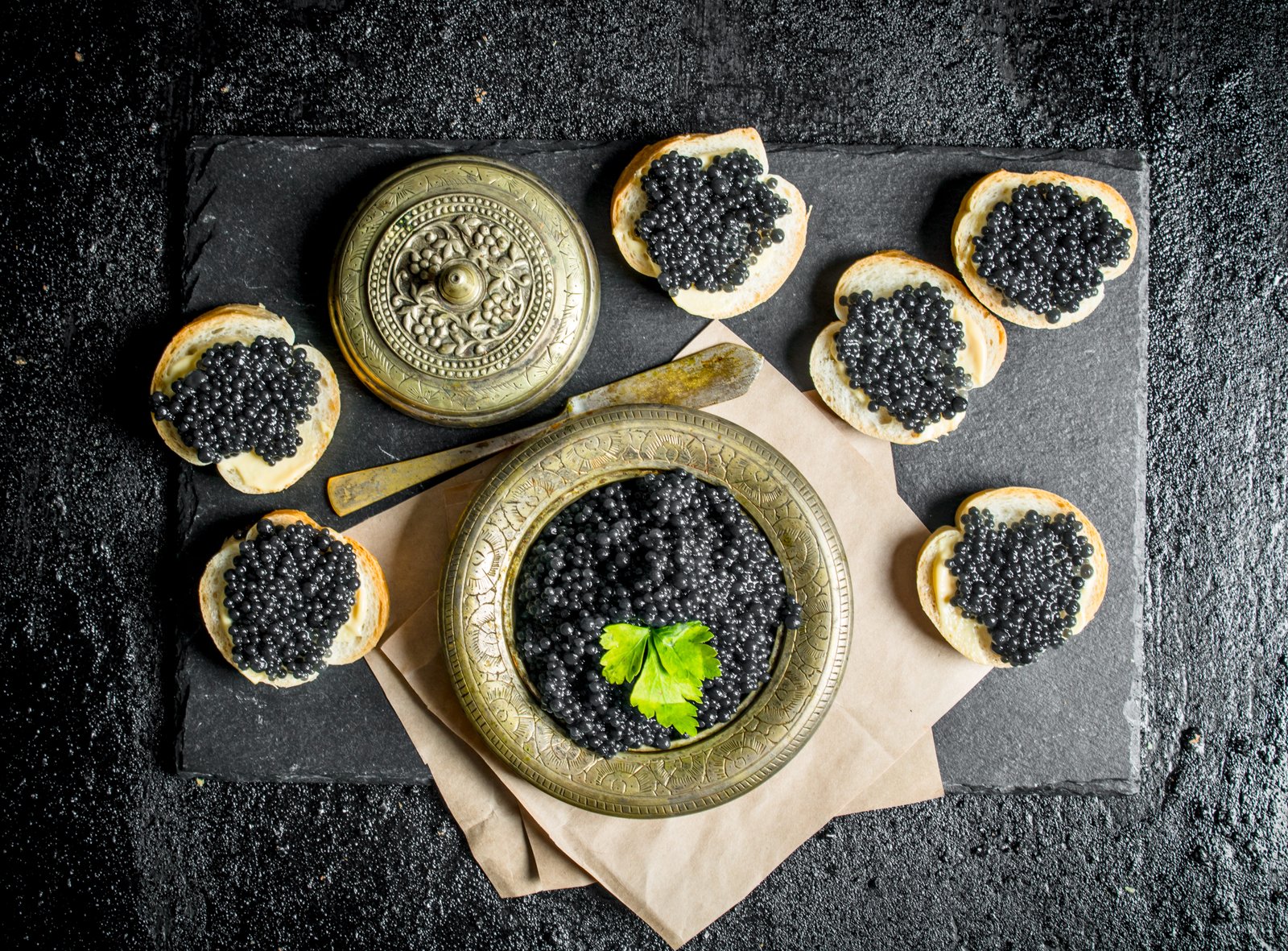 Sandwiches with black caviar and caviar in a bowl on paper with parsley.