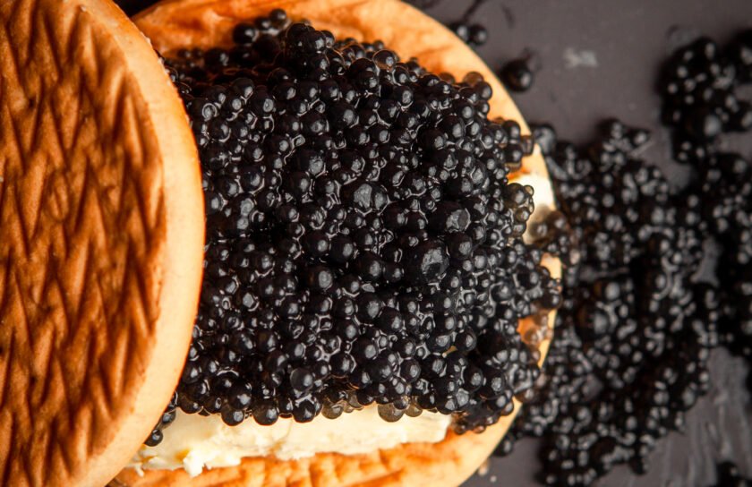 Set of butter and black caviar between biscuits on a dark background. top view.